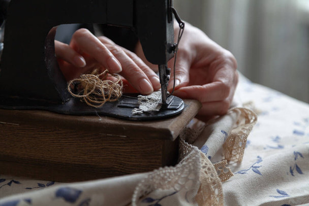 Handmade seamstress. Woman thin fingers hold the braid in a hand sewing machine close-up. Nearby lies a fabric with a blue patter - Zdjęcie, obraz