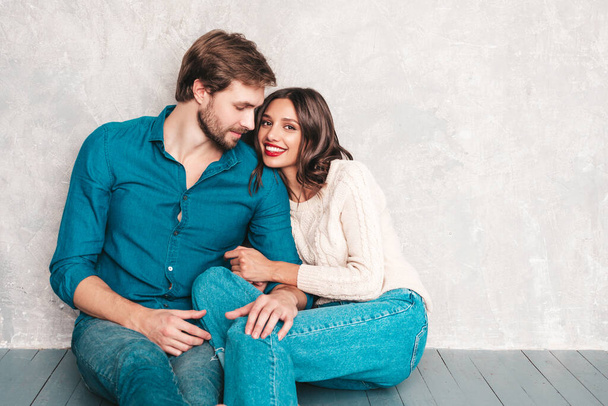 Smiling beautiful woman and her handsome boyfriend. Happy cheerful family sitting in studio on the floor near gray wall.Valentine's Day. Models hugging. Concept of love. Looking at each other - Foto, immagini