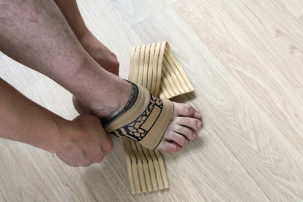 Mann Hände halten einen elastischen Verband Socke und legte es auf das Bein, um den Knöchel vor Verstauchungen zu schützen, Nahaufnahme - Foto, Bild