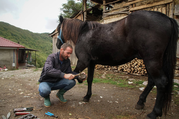 Η ακίδα αφαιρεί το μεγάλο νύχι. Ένας λαφυράνθρωπος δουλεύει πάνω σε άλογο για να το καθαρίσει πριν δημιουργήσει ένα πέταλο για το ζώο. - Φωτογραφία, εικόνα