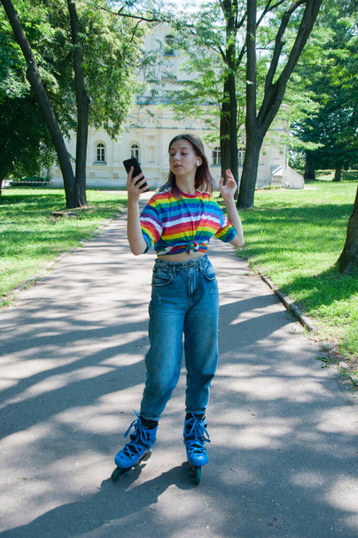 Zeer mooi meisje op rolschaatsen in hoofdtelefoon, met smartphone in een stadspark, luisteren naar muziek of praten - Foto, afbeelding