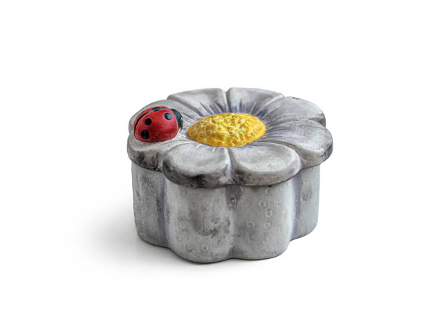 Grijze keramische doos, voor een waskaars, met een bloemvormig deksel en een lieveheersbeestje op het bloemblaadje. Doos geïsoleerd op een witte achtergrond - Foto, afbeelding