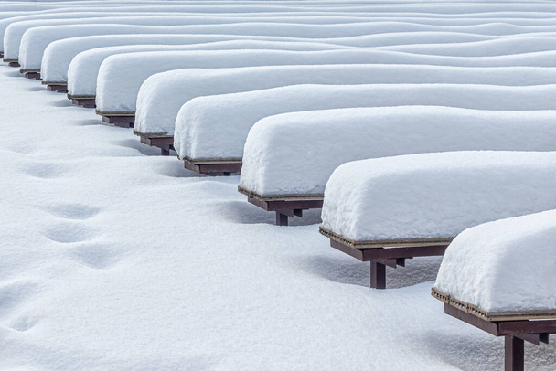 Χιόνι παρασύρεται στα παγκάκια, μετά από μια βαριά χιονόπτωση. Χιονισμένο υπαίθριο χώρο συναυλιών στο πάρκο της πόλης - Φωτογραφία, εικόνα