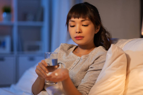 stressed asian woman taking medicine at night - Фото, изображение