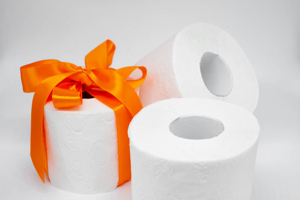 Vários rolos de papel higiênico perfurado branco. Um rolo é amarrado com uma fita de cetim laranja brilhante como um presente. - Foto, Imagem
