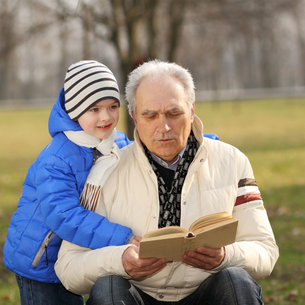 Дідусь і онук читають книгу на відкритому повітрі
 - Фото, зображення