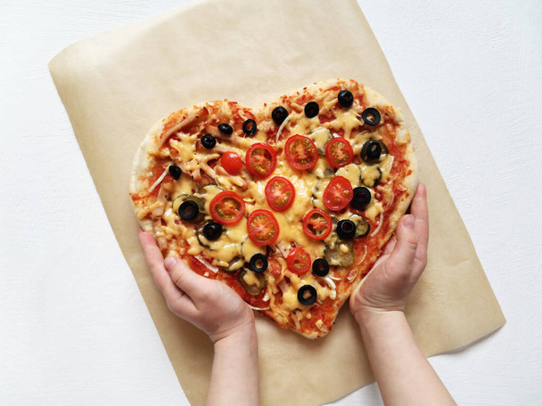 a child holds a heart shaped pizza made with his own hands. February 14 and moms day holiday concept - Valokuva, kuva