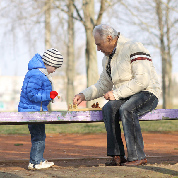 Nagyapa és unokája játék sakk a padon a szabadban - Fotó, kép