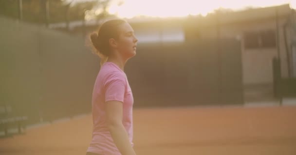 A lány fáradt a tenisz edzés alatt egy nyitott pályán, földfelülettel. lassan kiüti a labdát, és eltalálja egy fonákkal. - Felvétel, videó