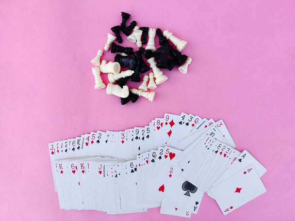 Κάτοψη. Κατάστρωμα καρτών παιχνιδιού και κομματιών σκακιού που απομονώνονται σε ροζ φόντο - Φωτογραφία, εικόνα