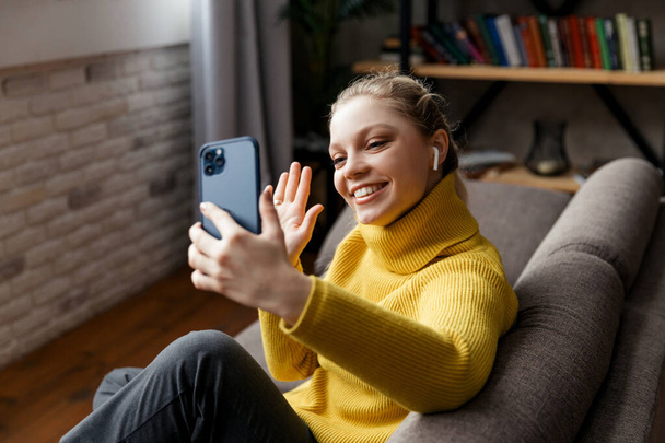 Νεαρή γυναίκα χρησιμοποιεί το τηλέφωνο σε βιντεοκλήση με τους φίλους της - Φωτογραφία, εικόνα