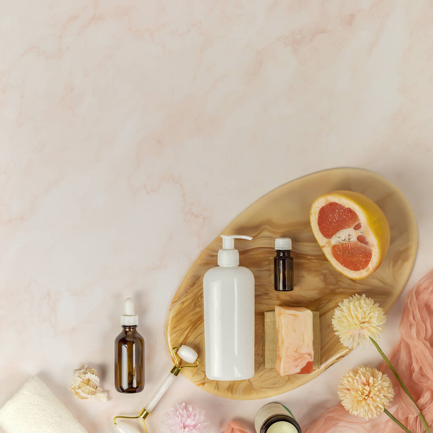 Cosmetic products and accessories for skin care, half a grapefruit and flowers on a pink background - Valokuva, kuva
