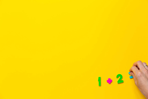 Прапор з математикою приклад один плюс два дорівнює руці на жовтому тлі, зробленому з дитячих пластикових номерів. Початкова освіта. Проста дія та рішення. Онлайн дистанційний курс. Мокап
 - Фото, зображення