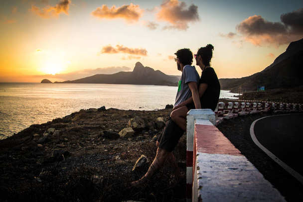 zwei Verliebte am Straßenrand, die den Sonnenuntergang am Meer beobachten - Foto, Bild