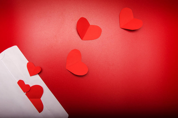 coeurs en papier origami rouge dans une enveloppe blanche isolée sur fond rouge. Saint Valentin, amour, concept d'anniversaire. Couché à plat, vue de dessus. Lettre d'amour romantique pour le concept de Saint-Valentin. - Photo, image
