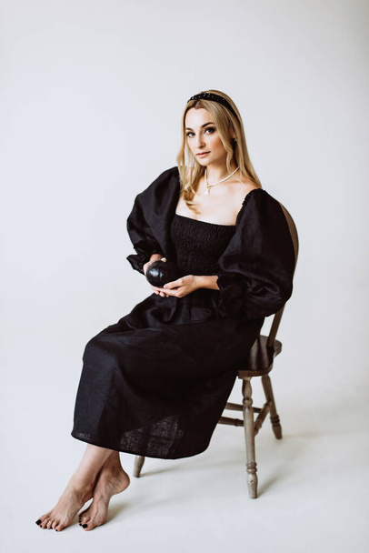 Beautiful Blond Woman in Black Linen Dress with a pumpkin in her hands. Ethnic fashion, natural fabric. Soft selective focus. - Фото, изображение