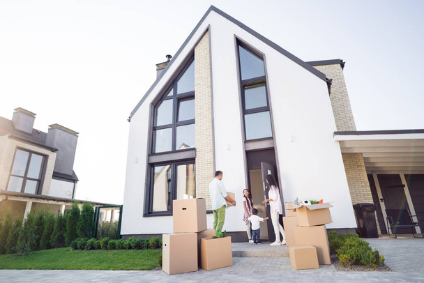 Photo portrait of full family moving to big modern house bringing in all their stuff in boxes outdoors in summer - Foto, Bild