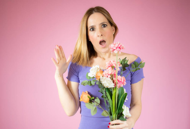 Портрет красивой молодой женщины, держащей большой букет цветов на розовом фоне. - Фото, изображение