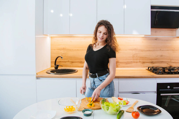 Una hermosa chica con una camiseta negra prepara una ensalada dietética en el fondo de una cocina ligera. Alimentación saludable. - Foto, Imagen