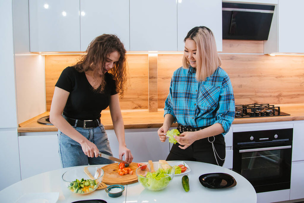 Dvě kamarádky připravují dietní salát na pozadí lehké kuchyně. Zdravé stravování. - Fotografie, Obrázek