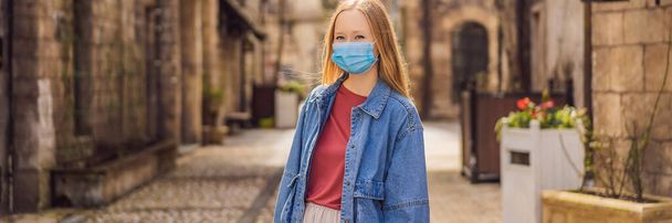 BANNER, LONG FORMAT Young woman wearing a medical mask during COVID-19 coronavirus tourist walks down the street in a European city after the end of COVID-19 coronavirus. quarantine - Fotoğraf, Görsel