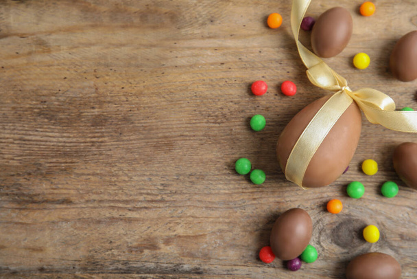 Lezzetli çikolatalı yumurtalar ve ahşap masada renkli şekerler, düz yatak. Metin için boşluk - Fotoğraf, Görsel
