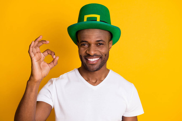 Portrait of positive afro american guy enjoy saint patrick celebration show ok sign wear green hat white t-shirt isolated over bright shine color background - Photo, Image