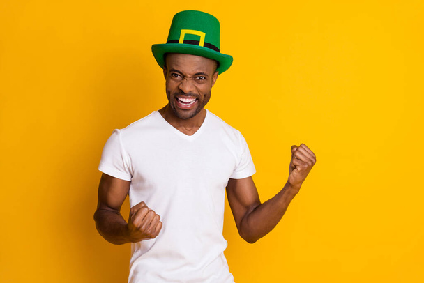 Portrait of delighted afro american guy win saint patrick contest raise fists scream yes wear green hat white clothes isolated over bright shine color background - Foto, imagen