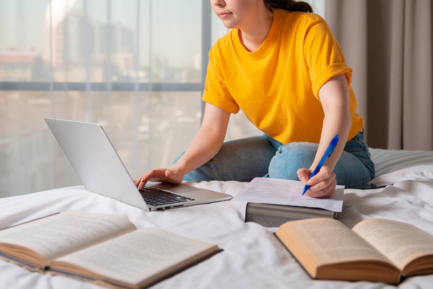 Het concept van online cursussen en online onderwijs. Een vrouw zit op een bed en werkt aan een laptop. Sluiten.. - Foto, afbeelding