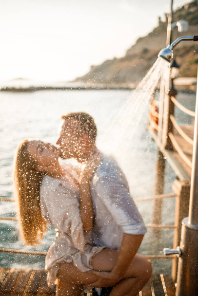Onnellinen pari meren rannalla. Mies ja tyttö ovat suihkun alla ulkolaiturilla. Onnellinen pariskunta lomalla. Mies ja nainen meren rannalla. - Valokuva, kuva