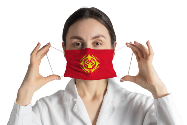 Respirator with flag of Kyrgyzstan Doctor puts on medical face mask isolated on white background. - Fotó, kép