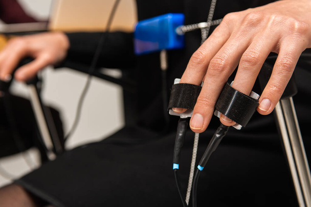 Close-up view of a suspect's hand connected to a lie detector / polygraph test machine while a male specialist conducts an interview - Photo, Image