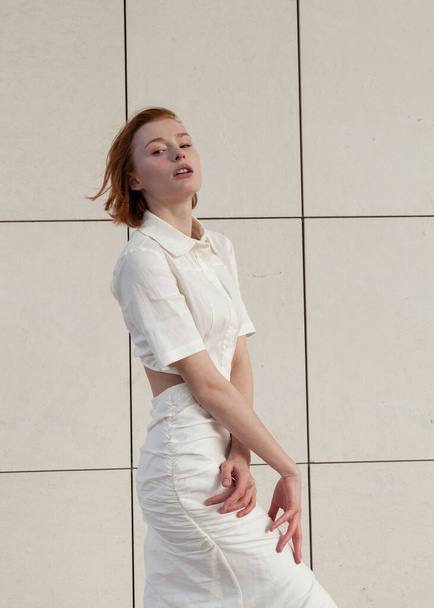beautiful and slender redhead girl in a white dress posing on the street - Φωτογραφία, εικόνα