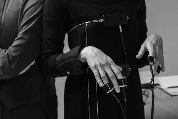 Крупный план руки подозреваемого, подключенной к детектору лжи - полиграфу, в то время как мужчина-специалист проводит собеседование. черно-белое фото - Фото, изображение