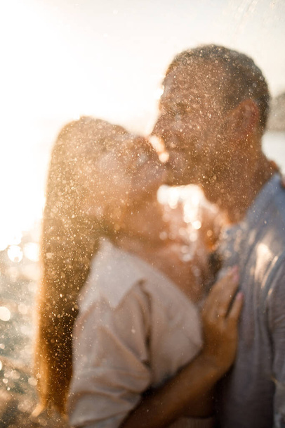 Красивая пара в любви обнимает и целует под струями воды в роскошном спа-отеле в свой медовый месяц, отпуск в тропиках. Селективный фокус - Фото, изображение