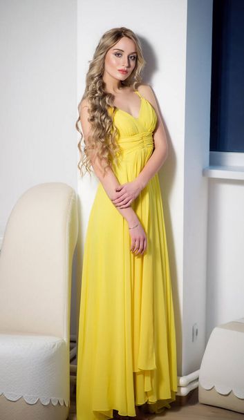 A young beautiful woman in a yellow evening dress. Beauty portrait of a model with a hairstyle - 写真・画像