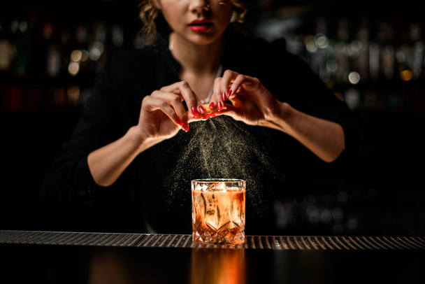 female bartender gently sprinkles on glass with cold alcoholic cocktail on the bar counter - Fotó, kép