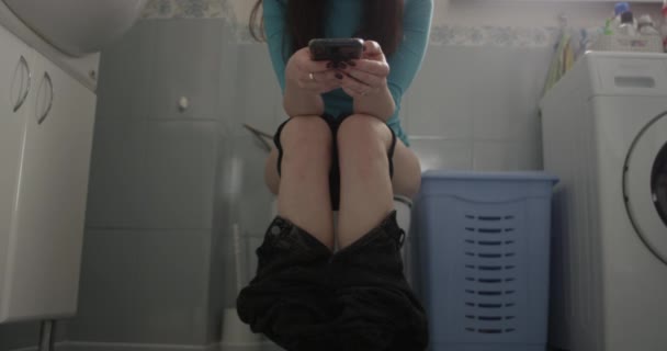 Egy nő ül a WC-n egy telefonnal a kezében - Felvétel, videó