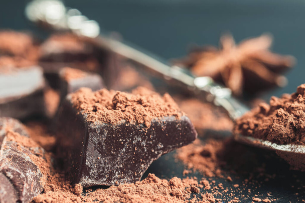 Trozo de chocolate, cubos de chocolate picados con cacao en polvo sobre fondo oscuro, vista de cerca. - Foto, imagen