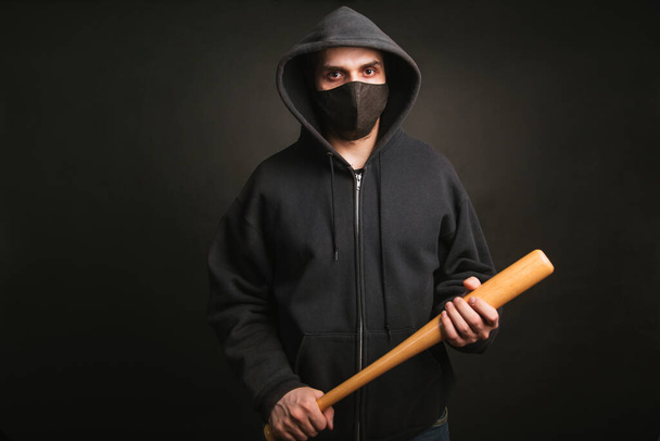 黒のスウェットと医療用マスクで強盗だ。野球バットを持つ危険な男と戦う準備ができています。彼は抗議に行く - 写真・画像