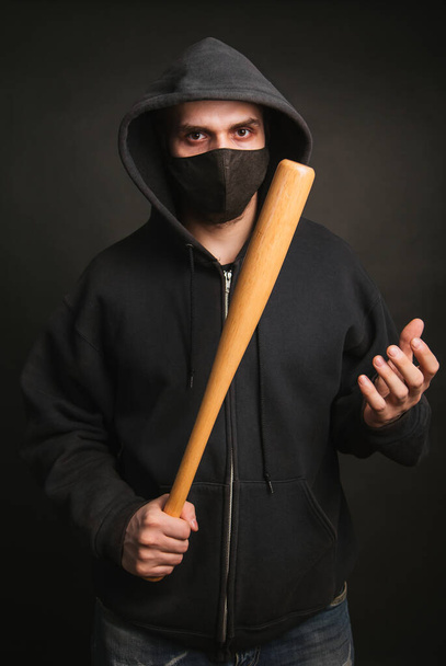 Bandido com uma camisola preta e uma máscara médica. Homem perigoso com um taco de basebol pronto para lutar. O tipo vai protestar. - Foto, Imagem