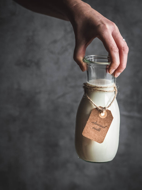 Female hand holding bottle of almond milk with paper label. Dark and moody. Copy space. - Foto, Imagen