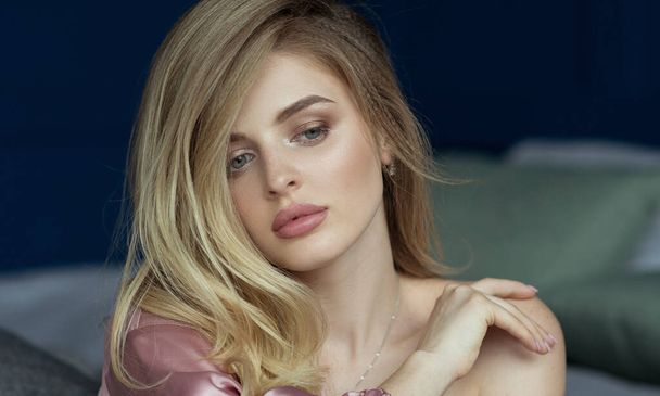Close-up portrait of young beautiful blonde woman with wavy hair in a pink peignoir with a plunging neckline. Text space - Photo, Image