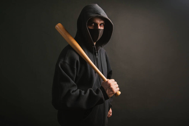 Bandit en sweat noir et masque médical. Un homme dangereux avec une batte de baseball prête à se battre. Il va protester. - Photo, image