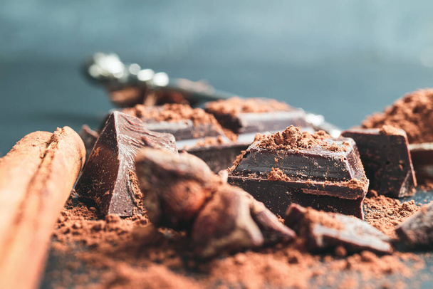 Cubos de chocolate picados con cacao en polvo y anís estrellado sobre fondo oscuro con espacio para copiar, vista de cerca. - Foto, imagen
