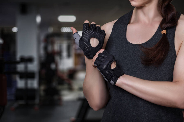 Femme met des gants de fitness sur le fond de la salle de gym. - Photo, image