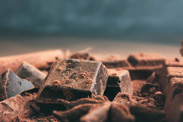 Gehackte Schokoladenwürfel mit Kakaopulver und Sternanis auf dunklem Hintergrund mit Kopierraum, Nahaufnahme. - Foto, Bild