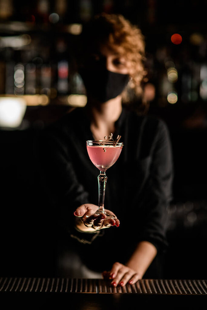 focus on beautiful glass of cocktail decorated with flower in the hands of woman in mask - Valokuva, kuva