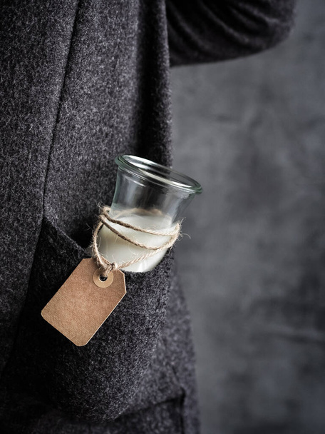Woman in black cardigan with bottle of almond milk with empty paper label in her pocket. Dark and moody. Copy space. Shallow depth of field. - Photo, Image