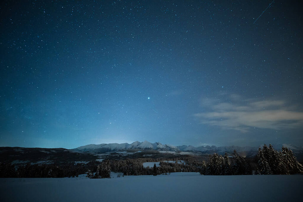 Śnieżna zimowa noc. Wspaniały nocny krajobraz. Niebo z gwiazdami nad śnieżnymi górami i doliną. Ciemna świąteczna noc. - Zdjęcie, obraz